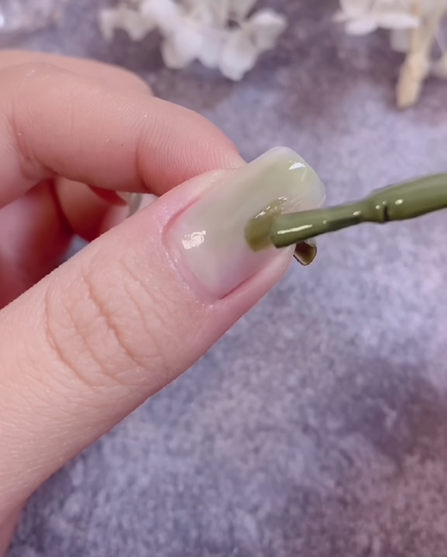Un pennello sfuma il gel color verde sulla superficie dellunghia per creare un effetto degradé.