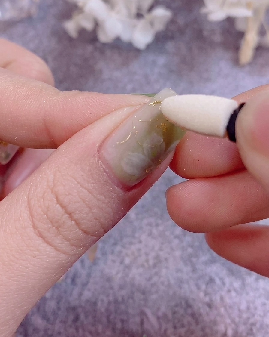 Un primo piano con pinzette che applicano delicati frammenti di foglia oro su ununghia dipinta.