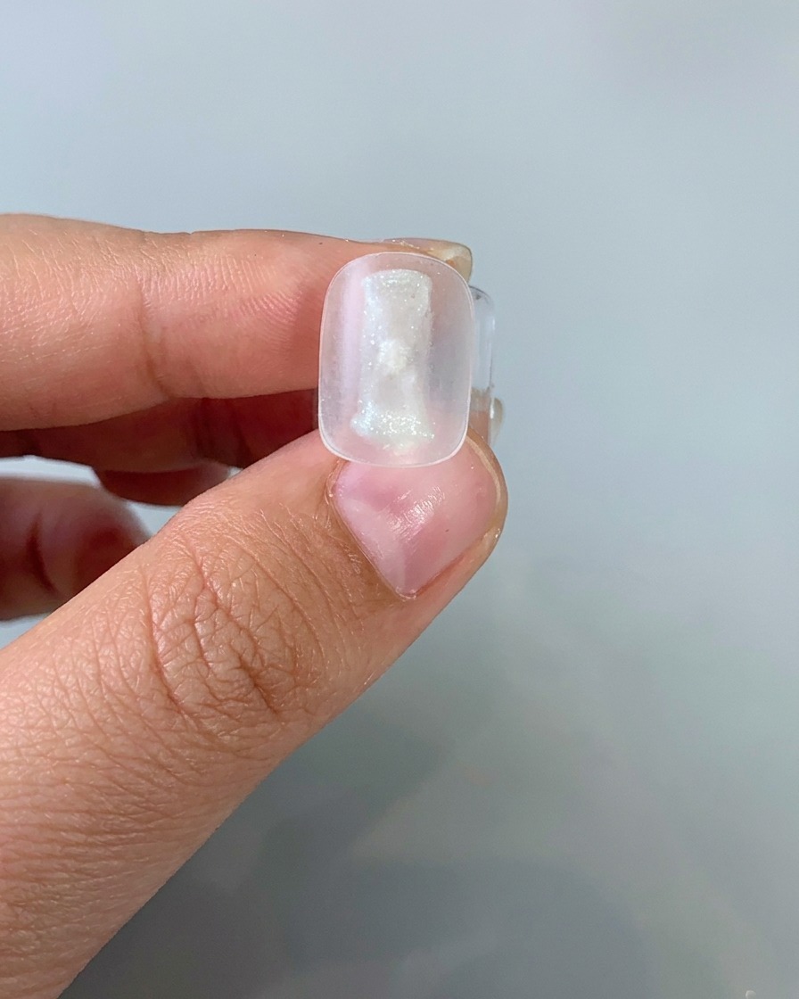 Un pennello che applica uno strato sottile di gel cat-eye chiaro su una tip.