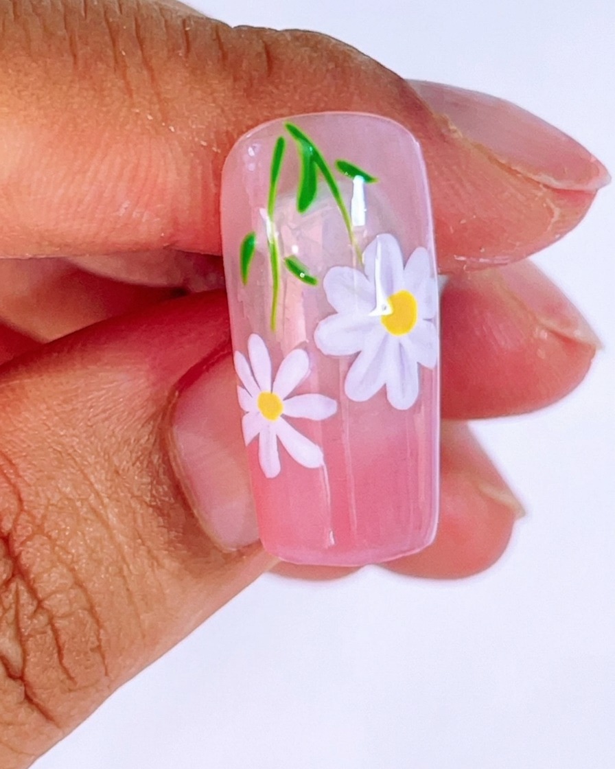 Primo piano di ununghia con base sfumata rosa su cui viene dipinta una seconda margherita più piccola con gel bianco e un pennello liner fine.
