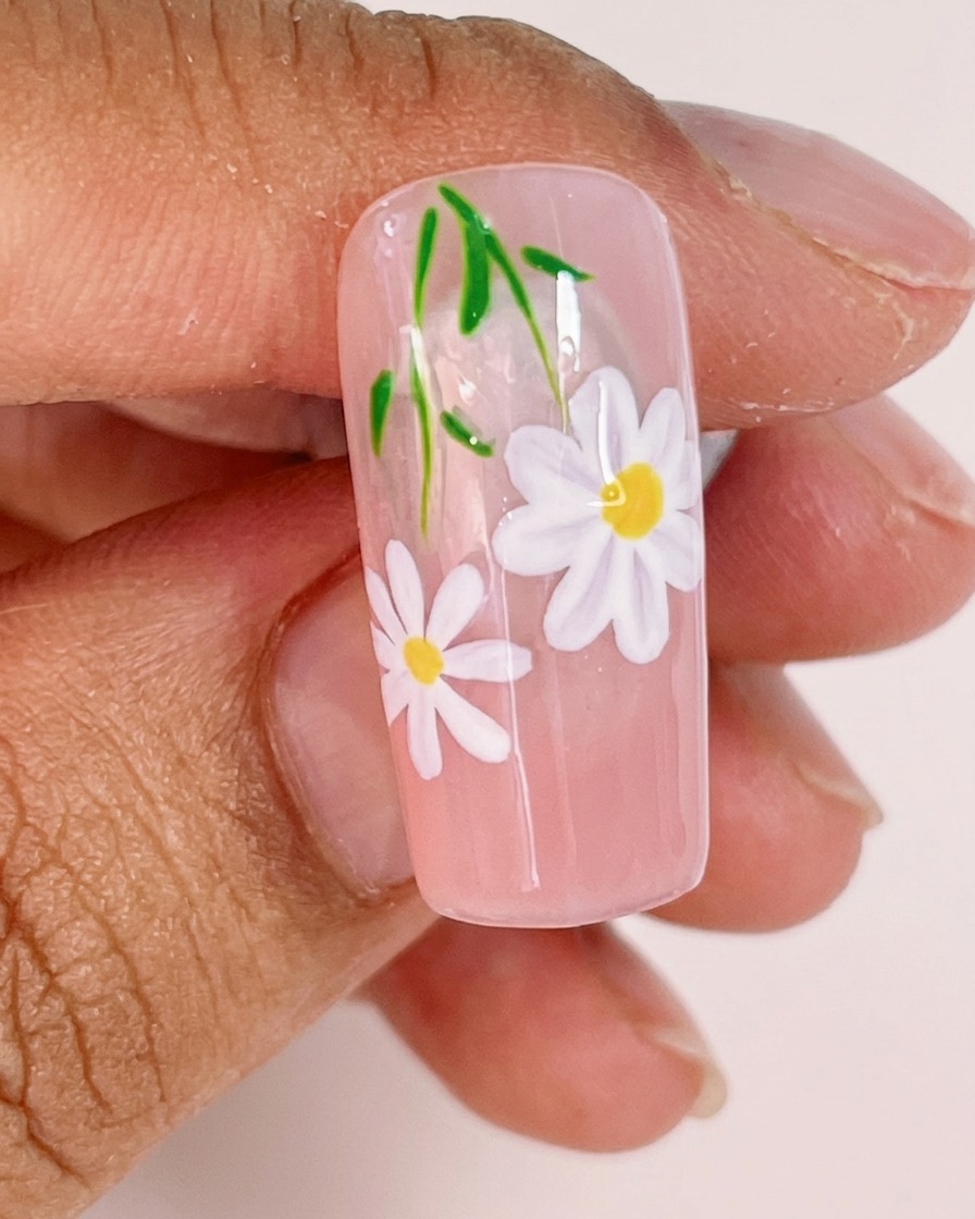 Un primo piano che mostra un pennello liner fine che aggiunge sottili steli verdi e piccole foglie al design della nail art a margherita.