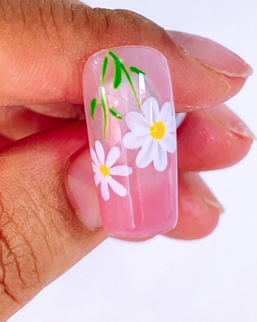 Un pennello che applica uno strato spesso e lucido di top coat trasparente sopra il design finito di margherite e foglie.