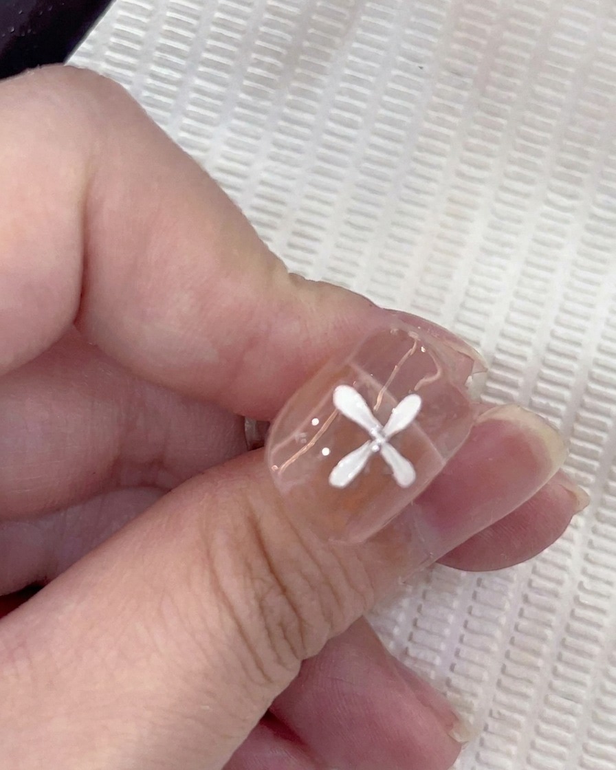 Un primo piano di ununghia con cinque petali bianchi dipinti in uno schema circolare, con un pennello che aggiunge un sesto petalo.