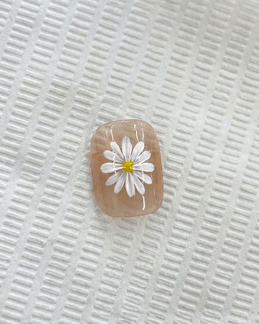 Un primo piano di una margherita bianca su ununghia, con un pennello per dettagli fini che applica un centro giallo.