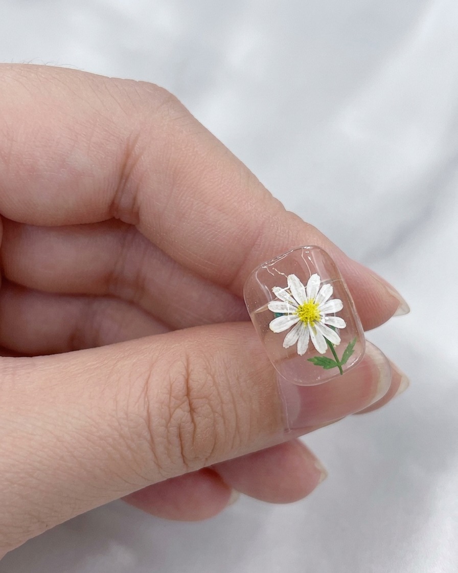 Un pennello che applica un top coat trasparente e lucido sopra un design di nail art con margherite finito.