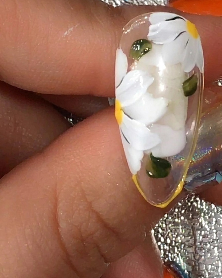 Un pennello che applica uno strato finale di top coat matte su ununghia con margherite bianche e foglie verdi.