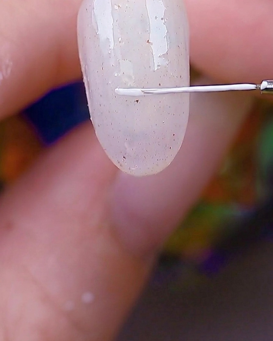 Dettaglio di un pennello liner sottile che traccia un bordo rettangolare bianco sullangolo di ununghia testurizzata.