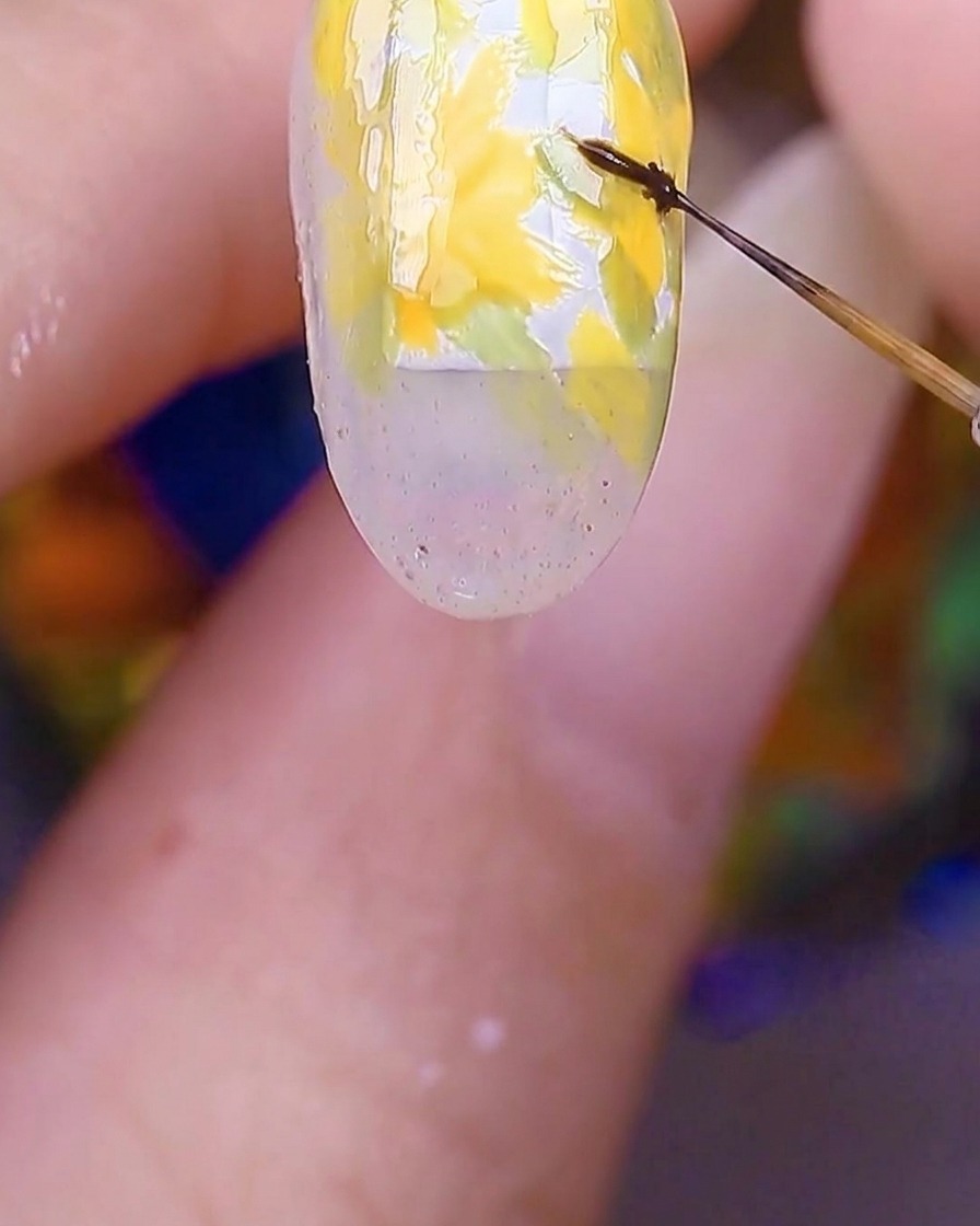 Un primo piano di ununghia che mostra i petali dei fiori gialli con un pennello fine che aggiunge minuscoli punti marroni proprio al centro.