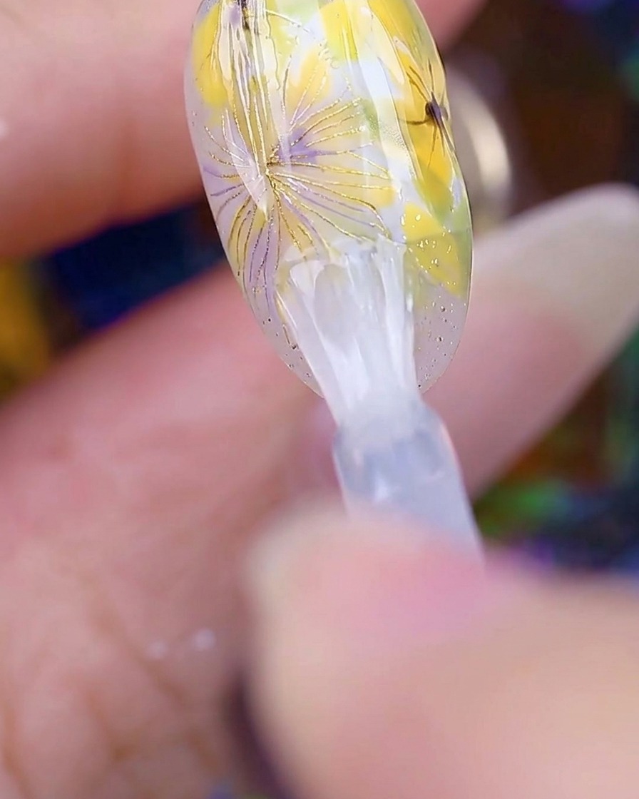 Un pennello che applica un top coat trasparente e lucido sulla nail art margherita completata, rendendo la superficie liscia e brillante.