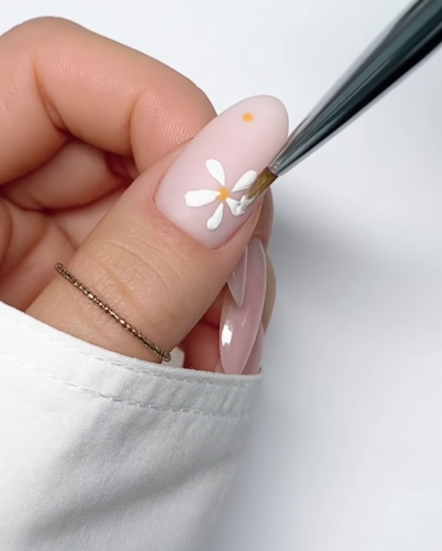 Primo piano di ununghia color nude con un piccolo punto di gel giallo perfettamente rotondo applicato sulla superficie, pronto per la pittura dei petali.