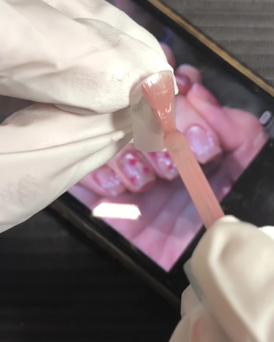 Un pennello applica smalto gel rosa nude su tutta la superficie dellunghia.