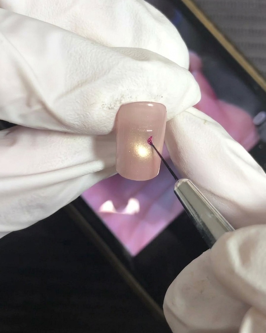 Un pennello a punta sottile applica con cura un punto di gel magenta al centro dellunghia.