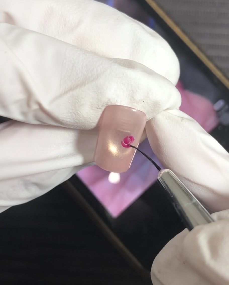 Un pennello a punta sottile aggiunge tratti a forma di parentesi attorno al centro magenta per formare i petali della rosa.