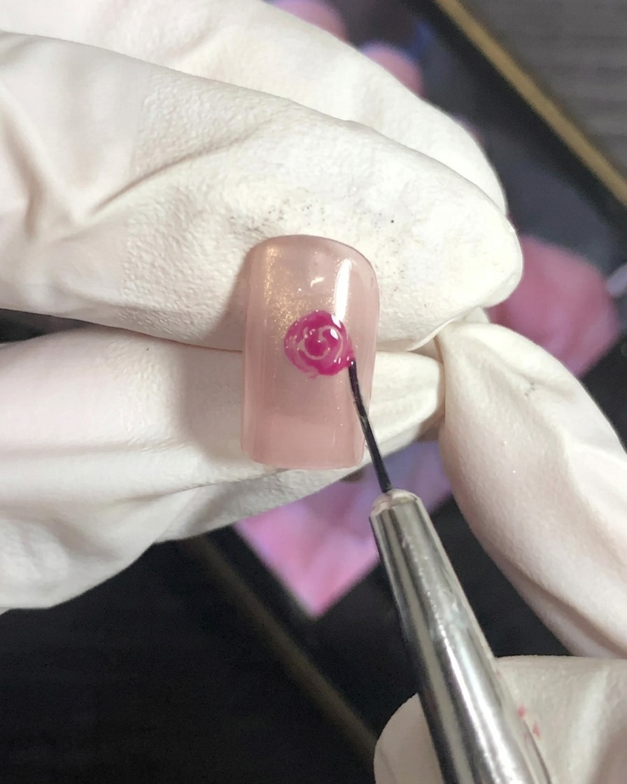 Un primo piano di un pennello per nail art che sfuma i bordi esterni di un design a rosa magenta su una base nude.