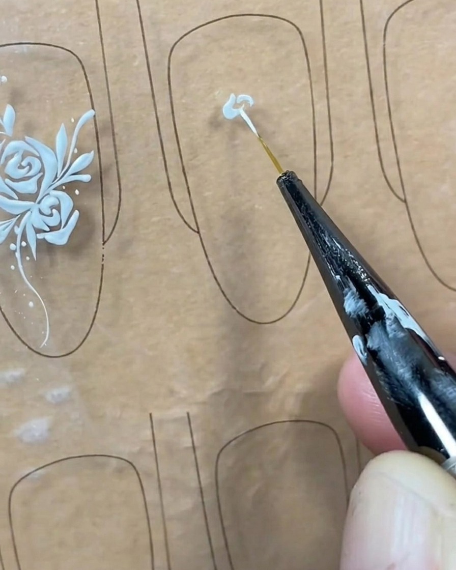 Primo piano di un pennello liner che applica un piccolo punto di gel bianco al centro di una tip trasparente.