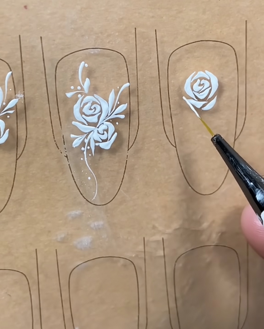 Primo piano di un pennello liner che aggiunge dettagli bianchi fini ai petali esterni di un design di rosa su una tip.