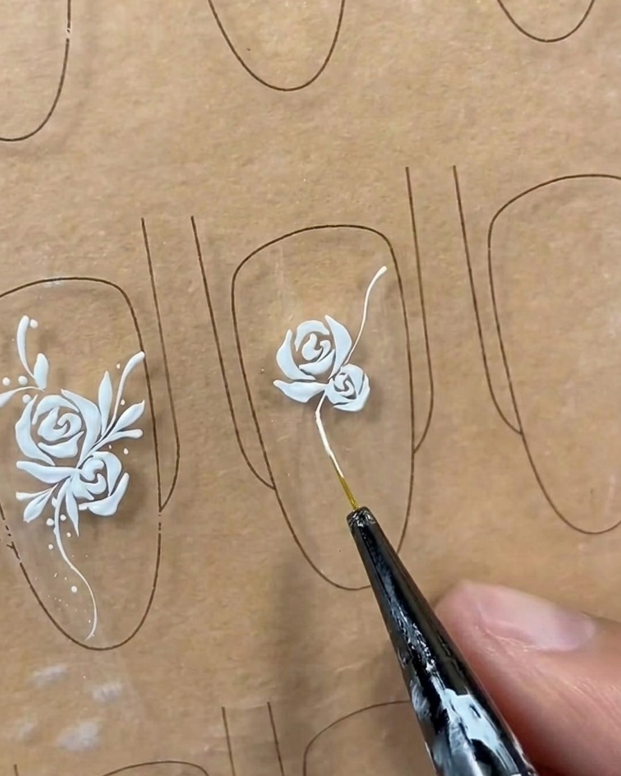 Una lunga linea di viticcio bianca e fluida disegnata dalla base di un design di rosa su una tip con un pennello liner.