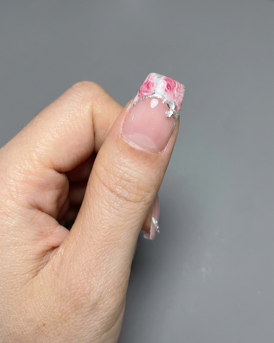 Un paio di pinzette che posizionano un adesivo con motivo a rosa su una punta francese ben curata.