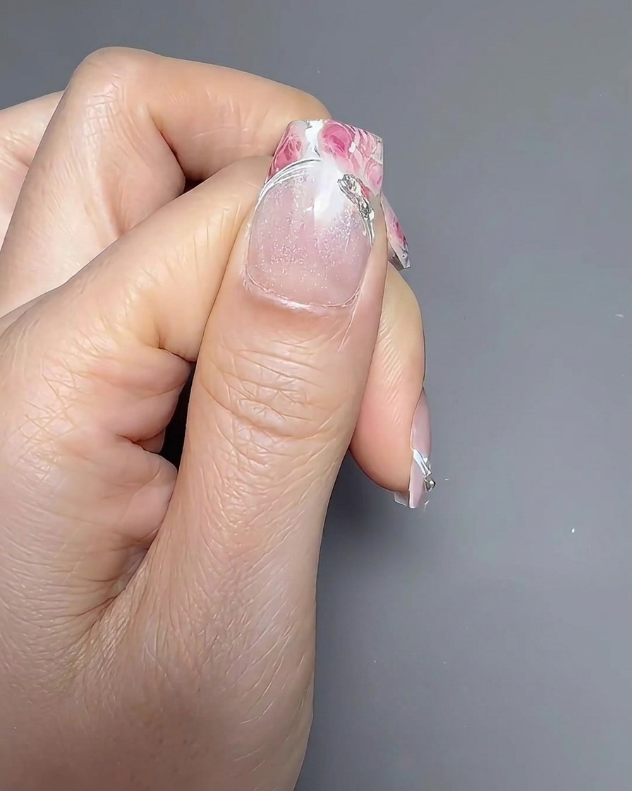 Un pennello per unghie che applica un top coat trasparente e lucido su ununghia decorata con motivi floreali.