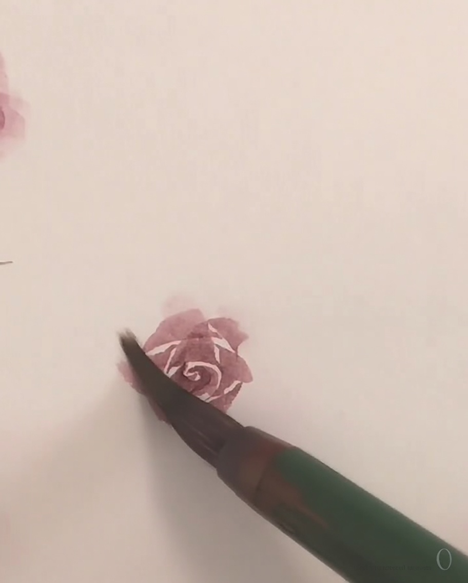 Un piccolo pennello che applica una delicata pittura rosa ad acquerello per formare il petalo esterno finale di una rosa.