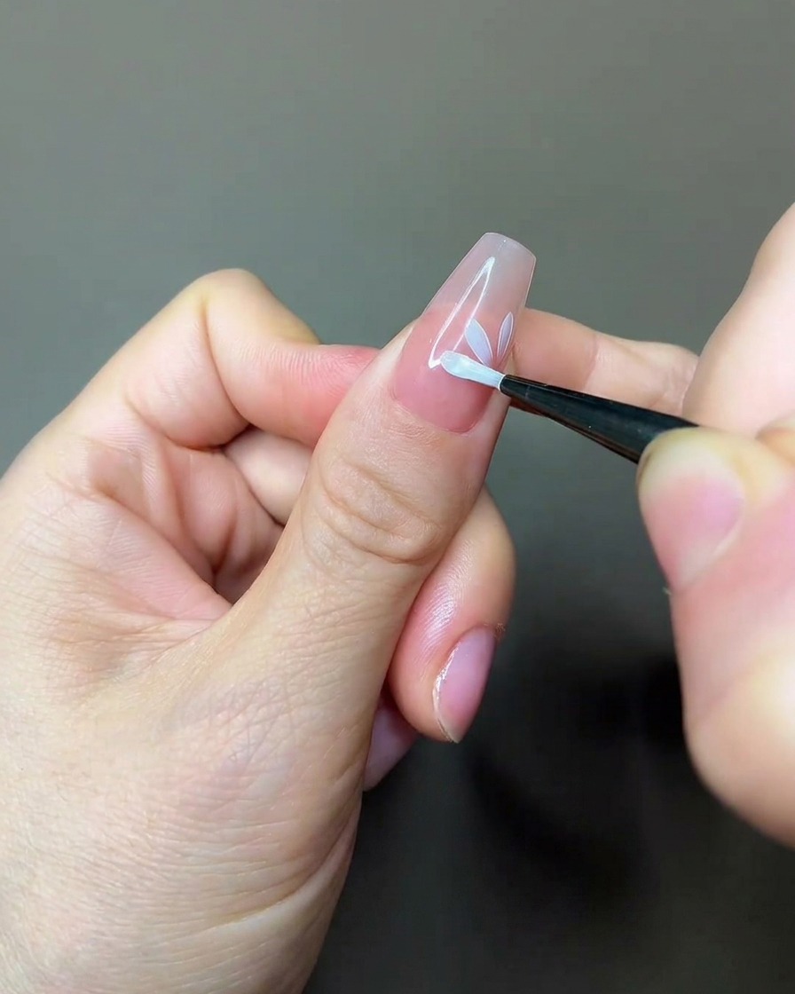 Un pennello per nail art che applica uno strato di top coat opaco sopra un design floreale parzialmente dipinto su ununghia nude.