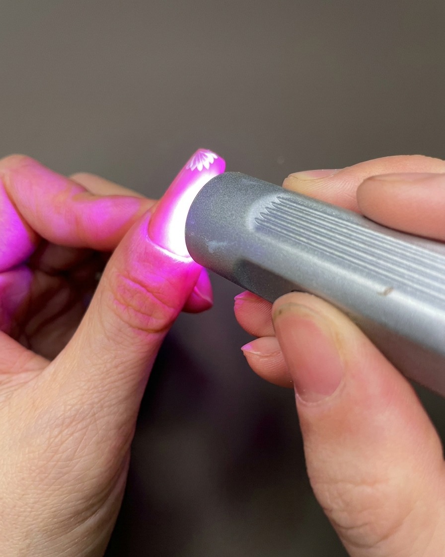 Uno strumento per nail art che applica una piccola goccia di gel scultoreo trasparente sulla superficie dellunghia vicino ai fiori dipinti.