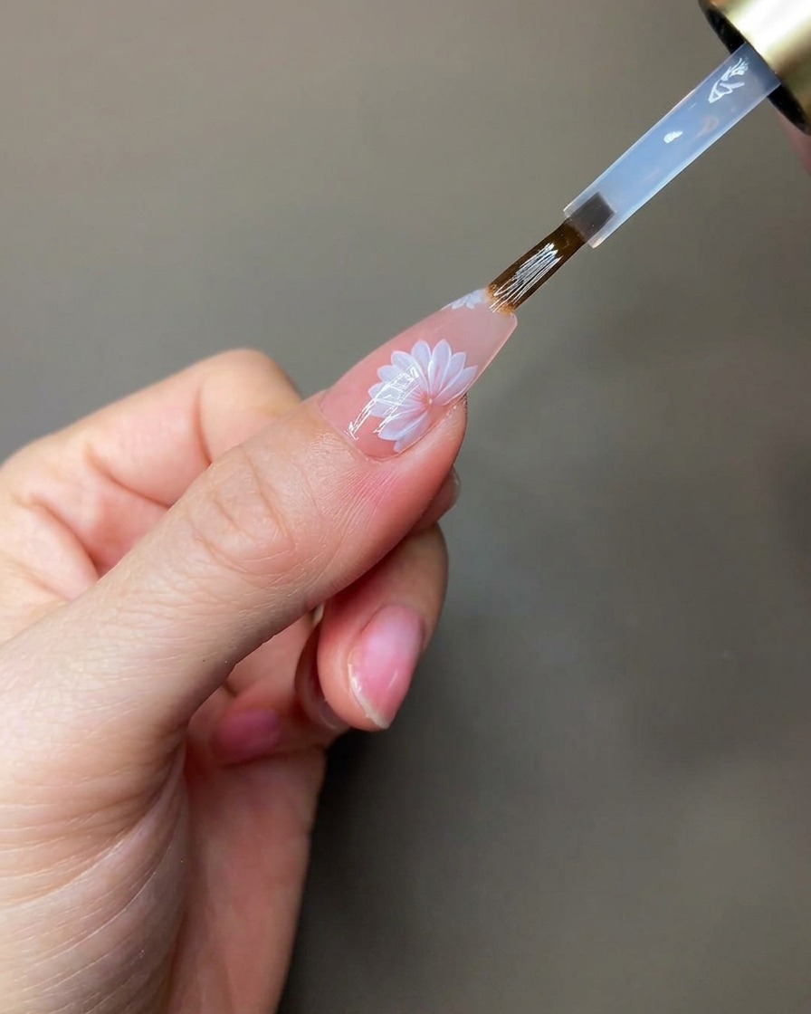 Una mano posizionata sotto una lampada UV/LED portatile mentre polimerizza i dettagli in gel scultoreo trasparente.