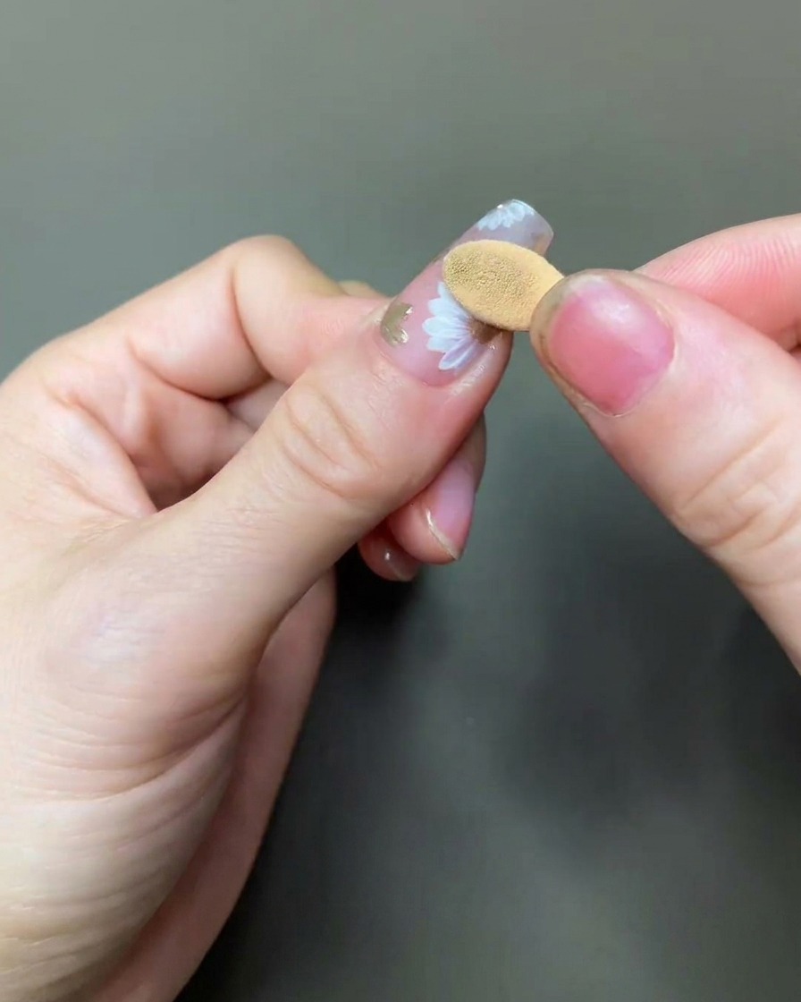 Un primo piano di un applicatore in spugna che strofina delicatamente il pigmento oro chrome sul centro di un design a margherita dipinto.