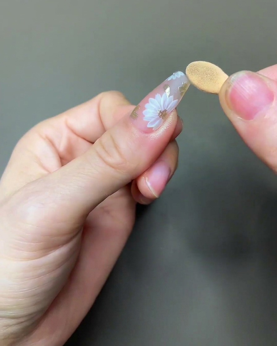 Un pennello che applica un top coat trasparente e lucido sopra la nail art completa con margherite e chrome.