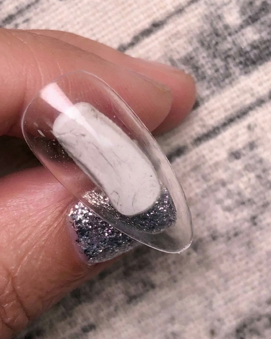 Un pennello applica un gel adesivo di trasferimento trasparente su una tip per unghie trasparente.