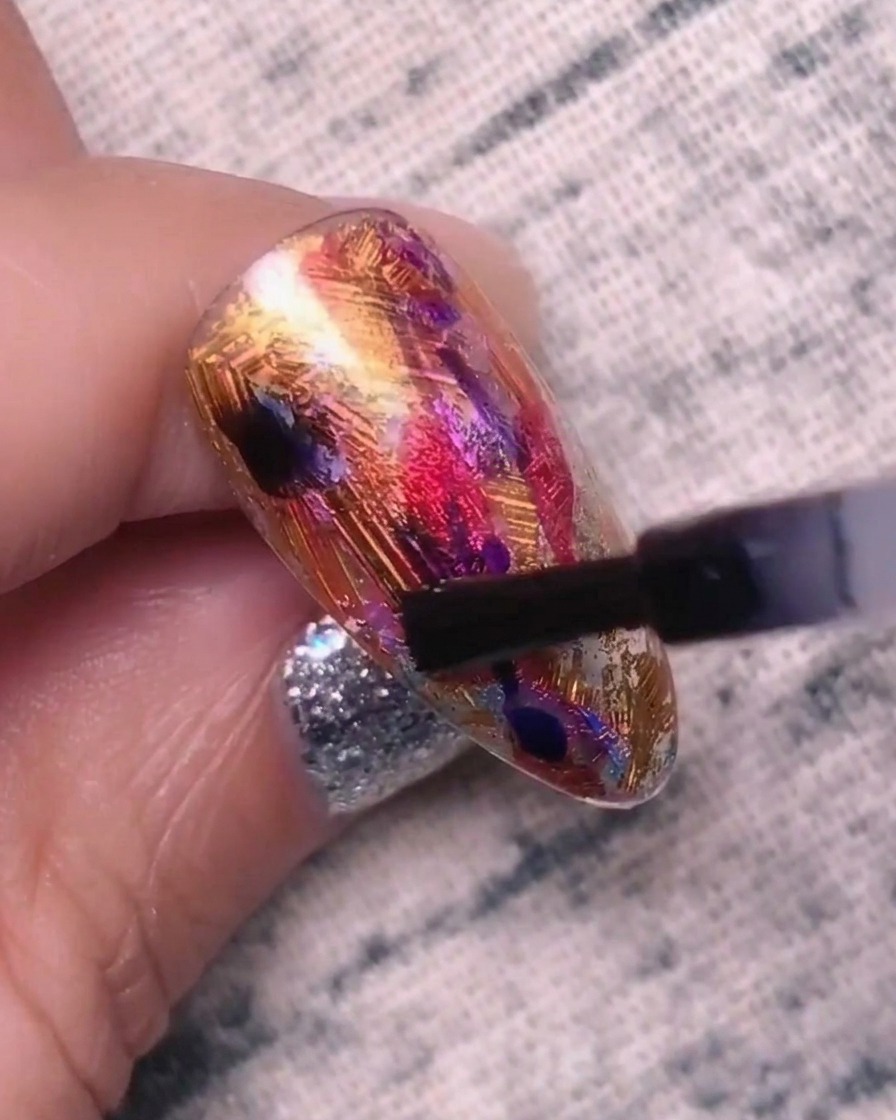 Un primo piano di ununghia punteggiata con gel blu-viola, che mostra i colori che iniziano a mescolarsi ed espandersi nello strato di base.