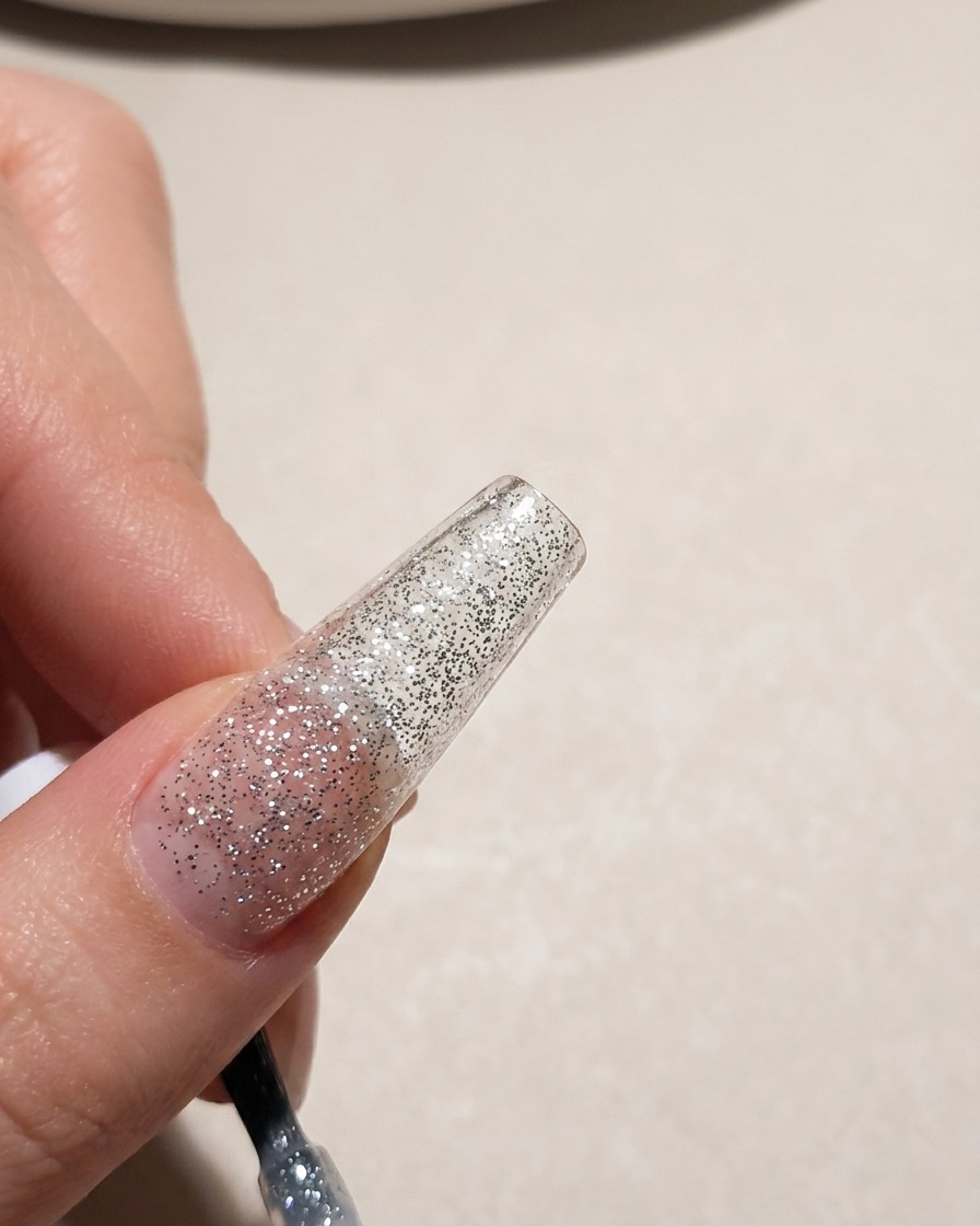 Una vista ravvicinata di una tip ungueale ricoperta da uno smalto gel glitterato color argento.