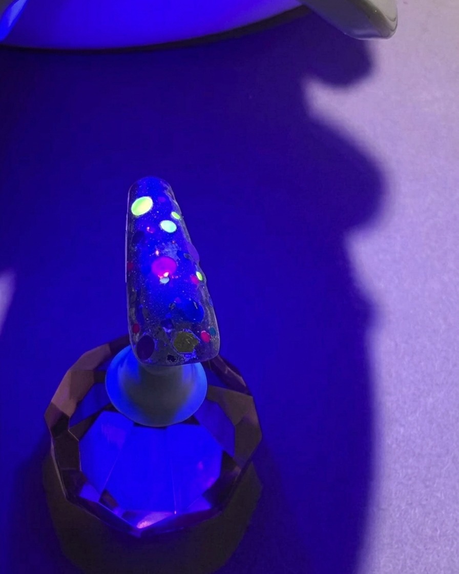 Ununghia con paillettes colorate sotto la luce viola di una lampada UV, durante il processo di polimerizzazione.