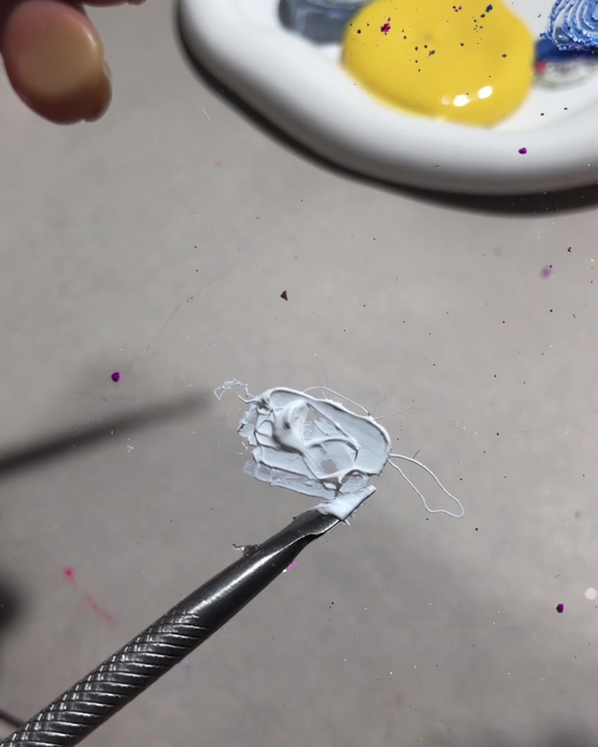 Un primo piano di uno strumento di miscelazione che amalgama gel da pittura bianco e gel alla frutta in una consistenza liscia e cremosa.