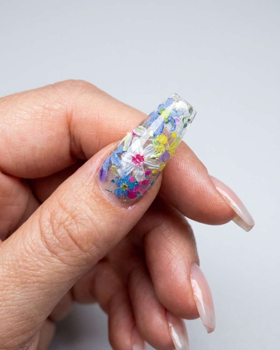 Una vista ravvicinata di un pennello che applica petali floreali 3D multicolori su una superficie ungueale decorata.