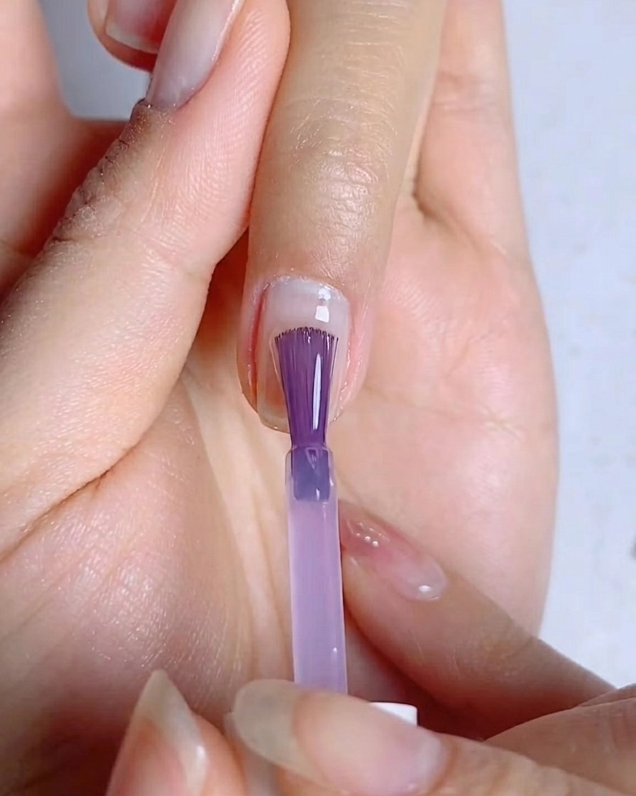 Un pennello da unghie che stende uno strato sottile e uniforme di smalto gel blu-viola sulla superficie dellunghia.