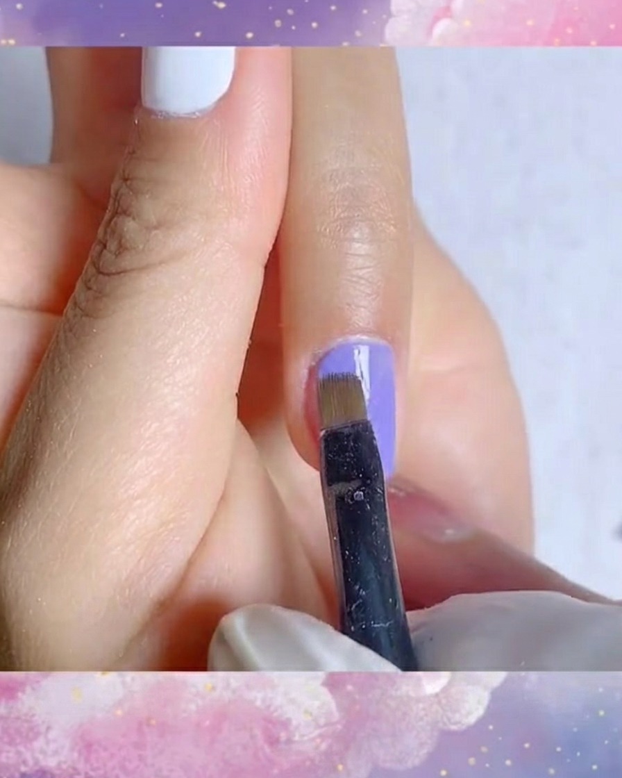 Un dettaglio in primo piano di un pennello a punta sottile che applica un secondo strato uniforme di vivace smalto gel blu-viola.