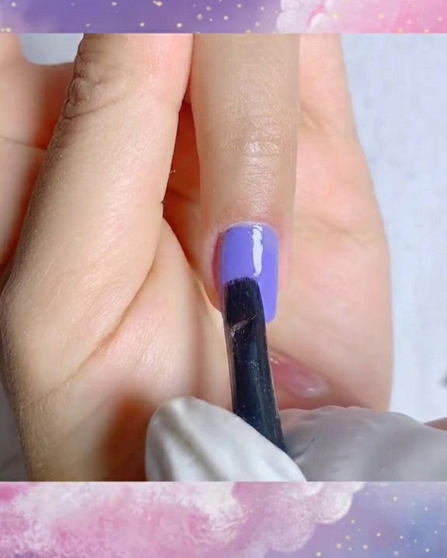 Uno scatto ravvicinato di un pennello a punta sottile che crea precisi tratti bianchi per i petali su una base gel viola.