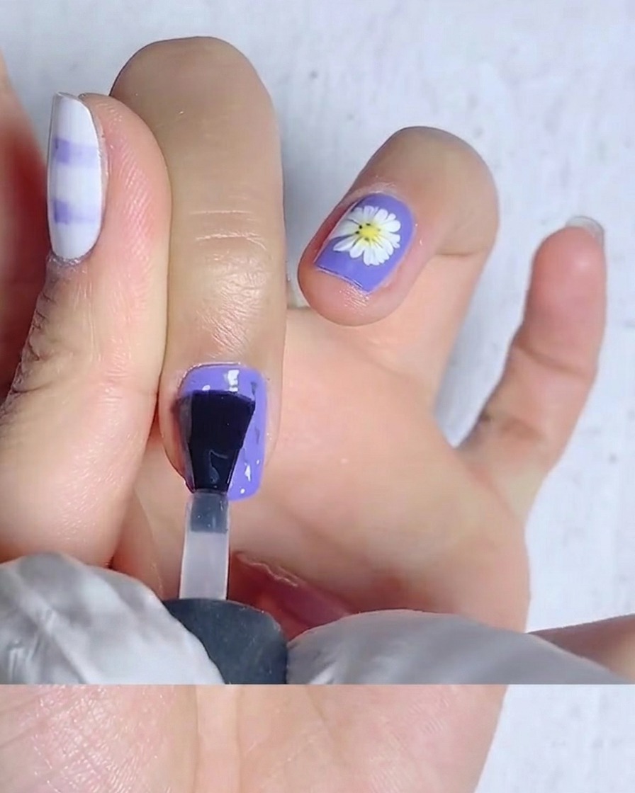 Un pennello da unghie che stende il top coat opaco su ununghia giallo brillante.