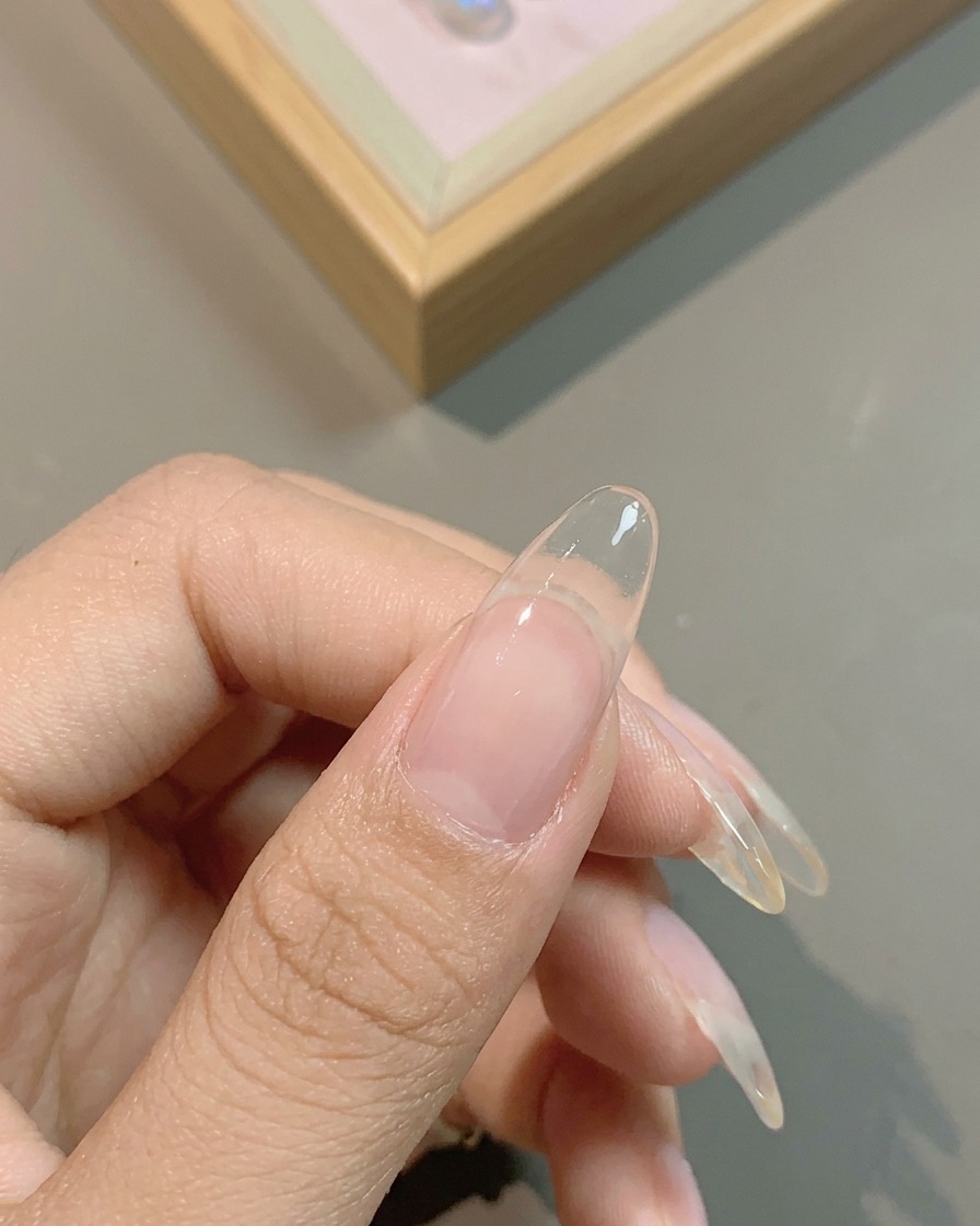 Un pennello applica una base coat gel bianco latte traslucido sullintera unghia.