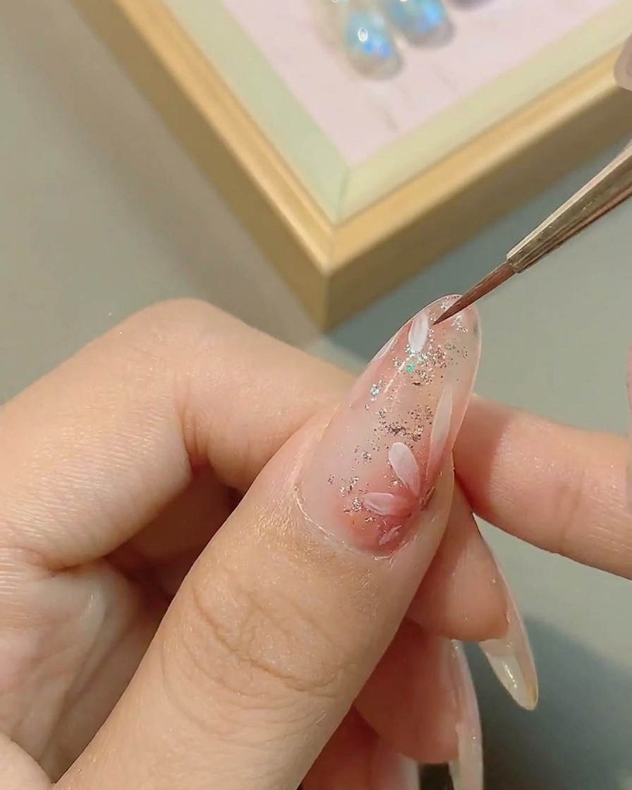 Un pennello applica un top coat trasparente lucido sopra la nail art a margherita finita.