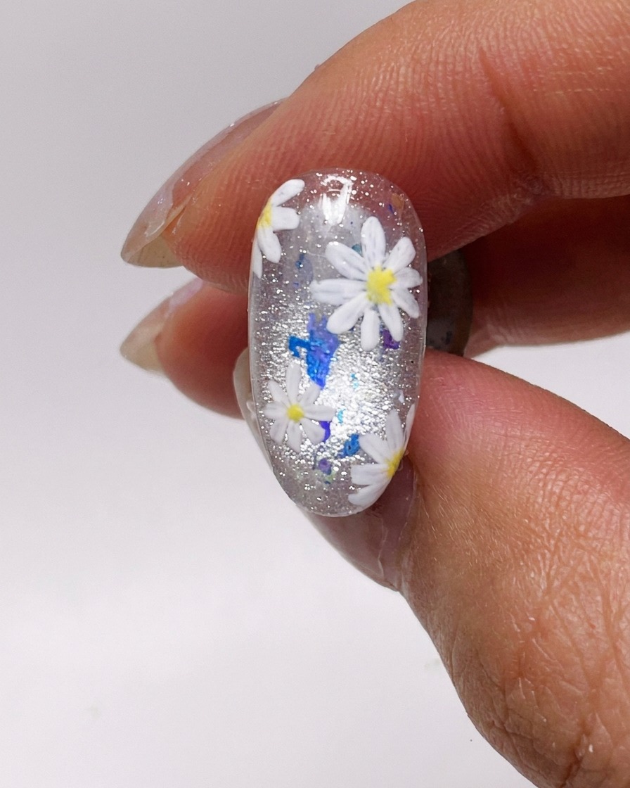 Un pennello applica uno strato sottile di gel cat-eye argento su ununghia naturale.