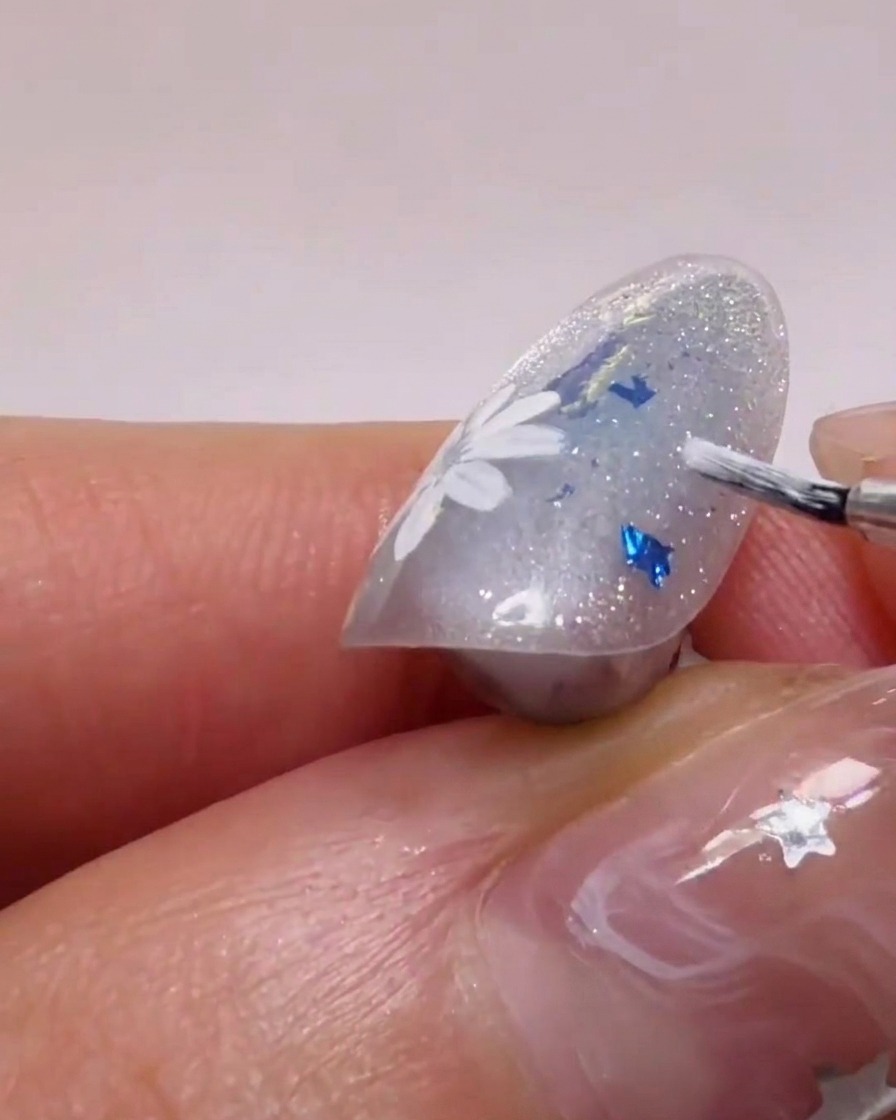 Un pennello da nail art applica gel bianco per formare petali su una base glitterata.