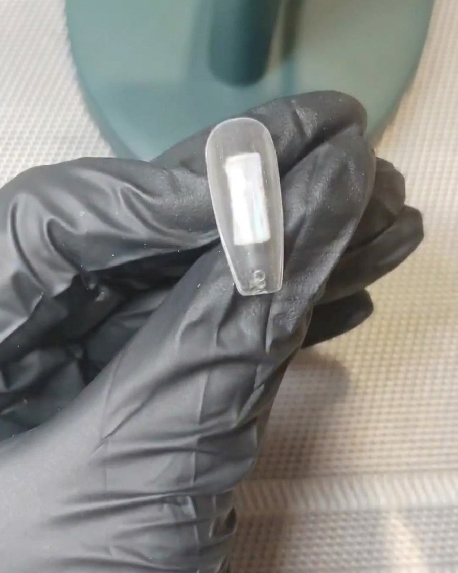 Un primo piano di una tip trasparente con puntini distinti di gel rosa nude e bianco lattiginoso posizionati al centro della superficie.