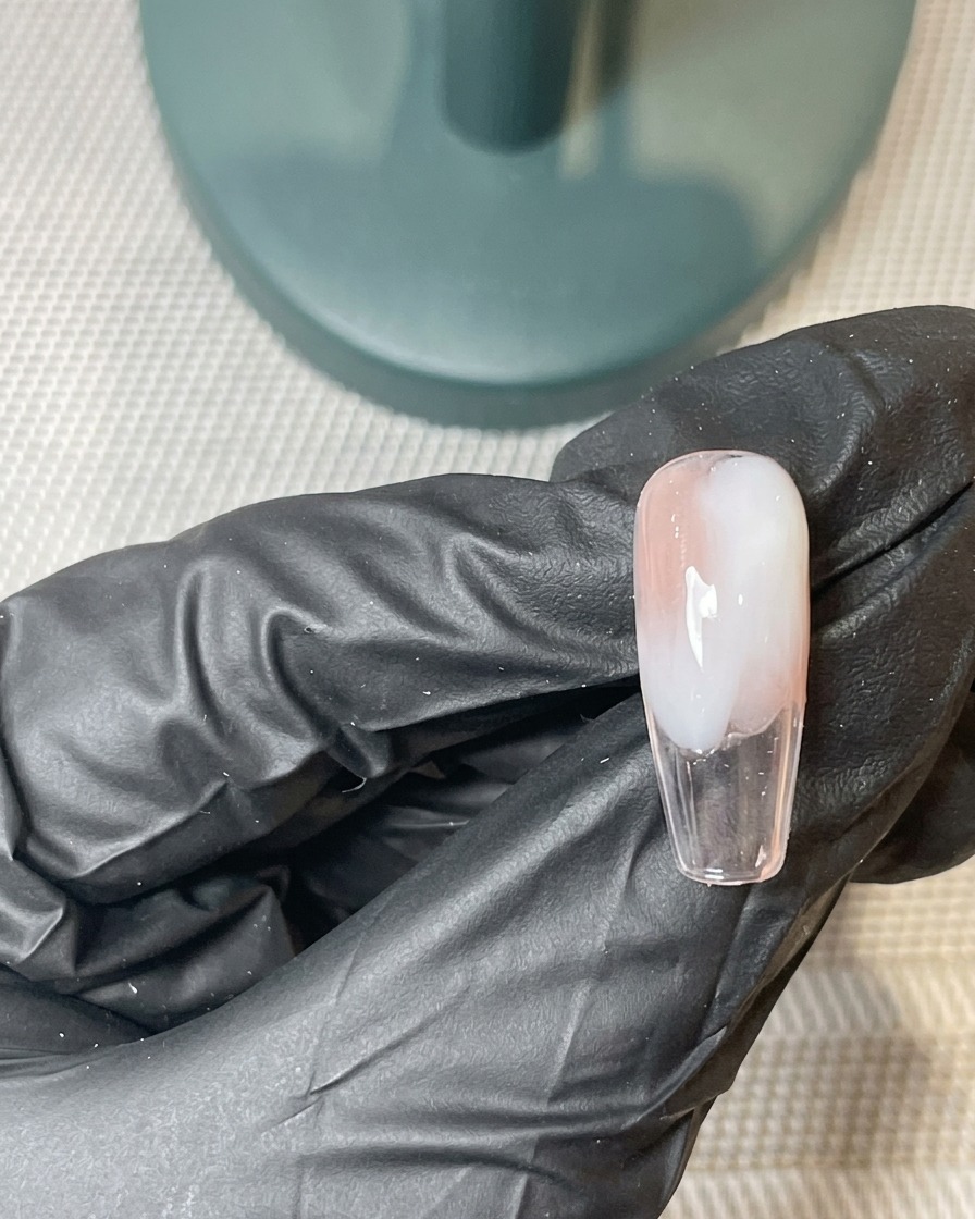 Un pennello che applica un secondo strato sottile di gel rosa e bianco sopra la base ombré precedentemente polimerizzata.