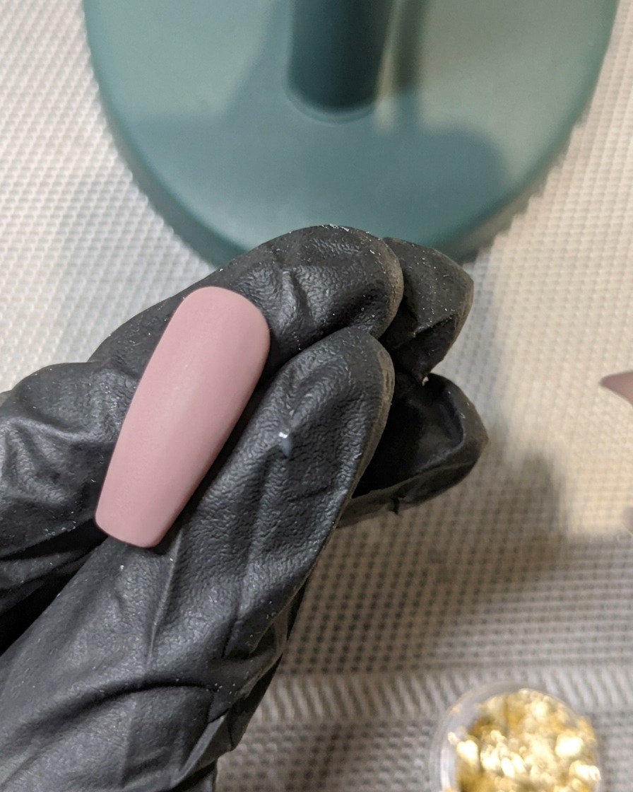 Un pennello che applica uno strato di top coat opaco su ununghia decorata con foglia doro.