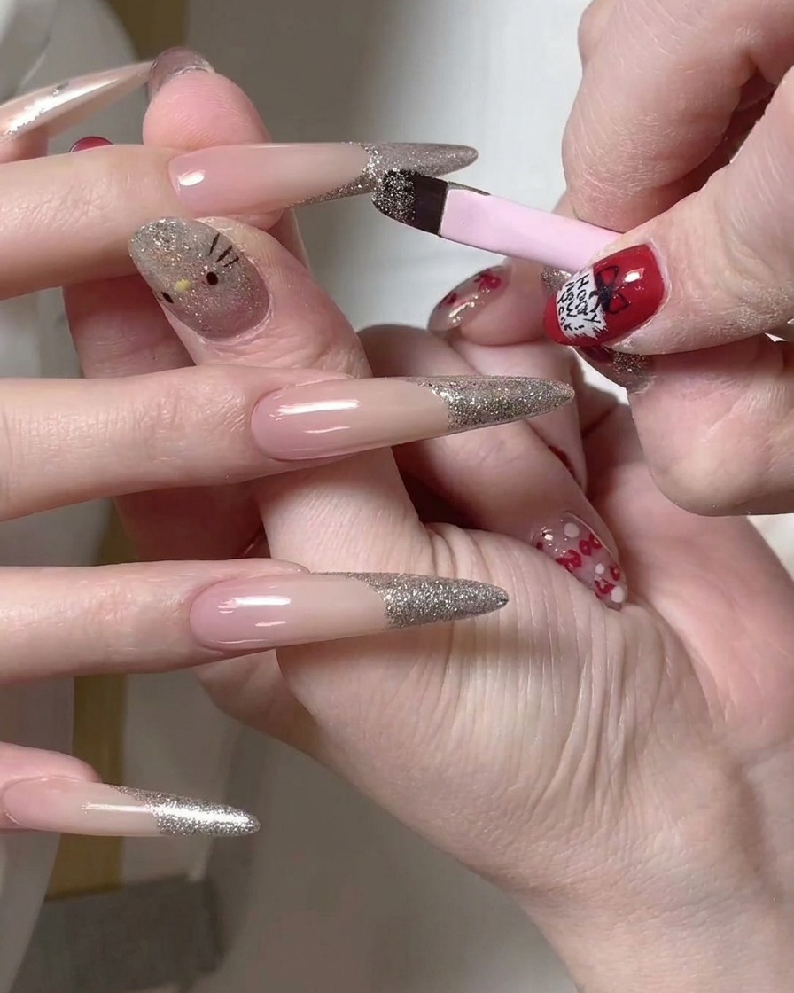 Un pennello a punta sottile utilizzato per rifinire il bordo di una french glitter argento su ununghia lunga.