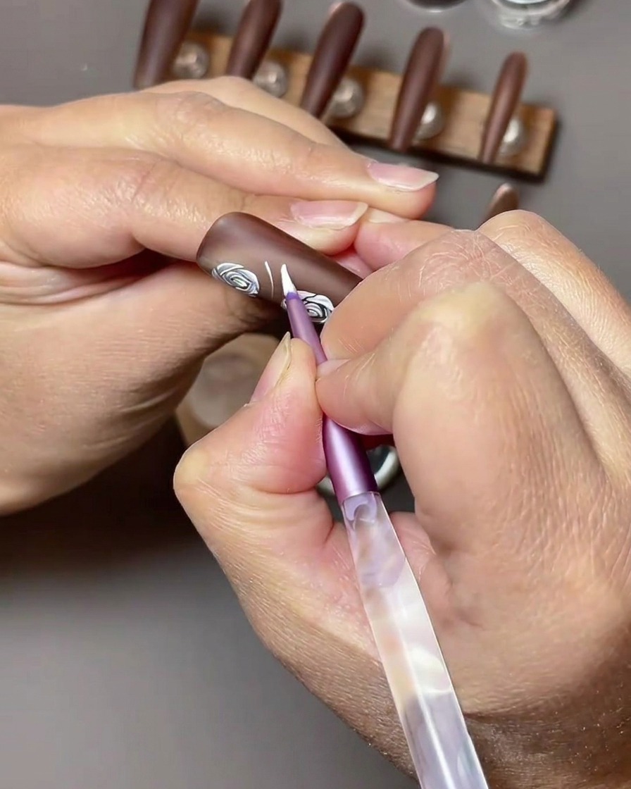 Una vista ravvicinata che mostra il gel per nail art bianco usato per dipingere forme di foglie accanto alle rose bianche esistenti su ununghia marrone.