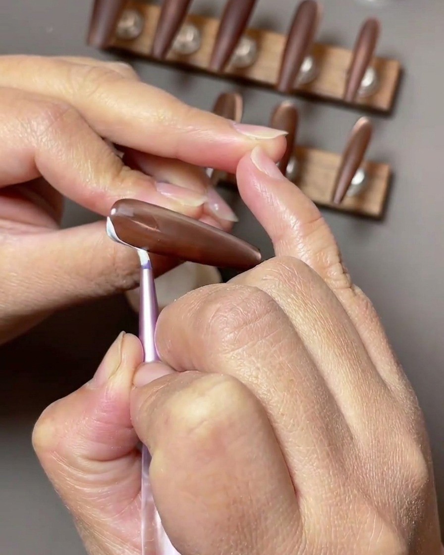 Primo piano di ununghia marrone dove vengono dipinti delicati tratti bianchi simili a nastri lungo il lato della superficie dellunghia.