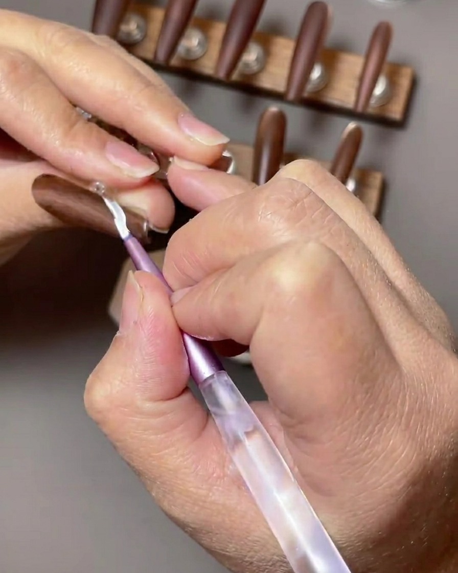 Un primo piano di ununghia marrone accentuata da un design french tip bianco applicato con un pennello sottile da nail art.
